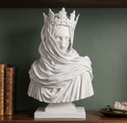 Busto bianco effetto gesso di regina velata con corona su mensola in legno tra libri antichi e cristalli