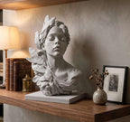 Busto in gesso bianco di figura femminile con foglie su mensola in legno accanto a libri