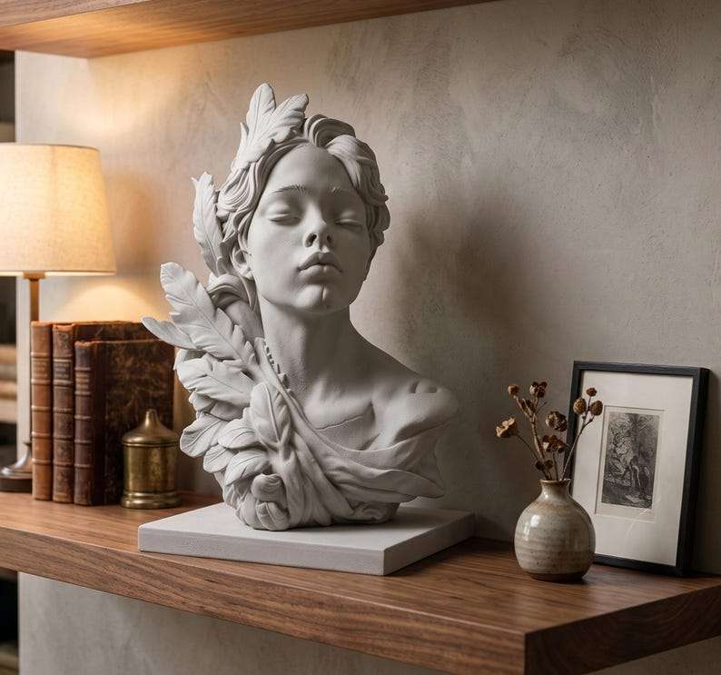 Busto in gesso bianco di figura femminile con foglie su mensola in legno accanto a libri