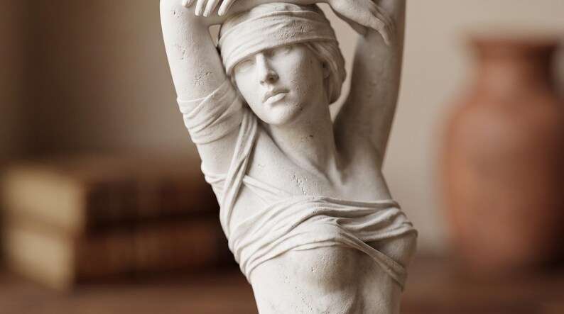 Primo piano del viso bendato e del busto drappeggiato della scultura bianca effetto gesso